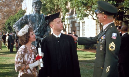 Gump's mother, played by Sally Field; Gump; and a military officer stand outside as Gump wears a black cap and gown
