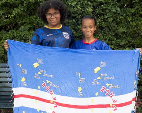 Two young people hold up a Cape Verde flag in front of greenery