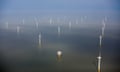 Rows of white wind turbines in rows stretch back across a seascape partly lit by sunlight