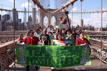 A group of people march along a bridge, with a row of people in front carrying a green banner reading ‘Tear down fossil fuels’