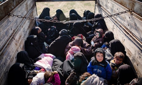 Picture of women and children sitting crowded in the back of a high-sided open truck, some of them looking at the camera
