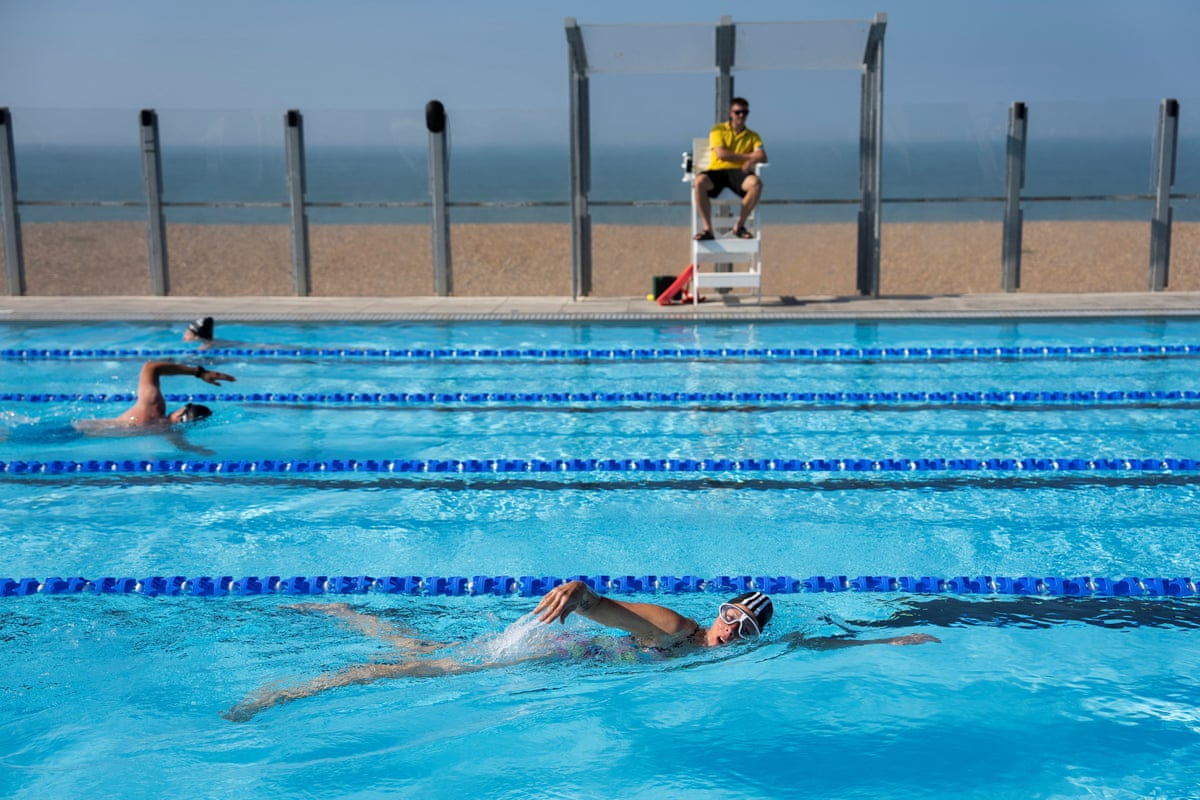 People swimming in an open-air pool with a view of the beach and sea