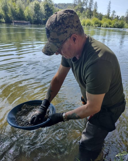 Minto in waders in a knee-deep river, sifting through silt