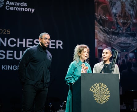 Three people on stage at the award ceremony behind a podium, with Esme Ward giving a speech