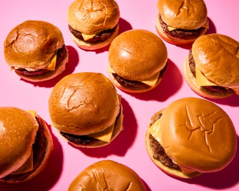 Multiple cheeseburgers with cheese and patties on golden buns arranged on a pink background