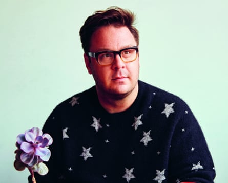 MasterChef winner Tim Anderson wearing a dark blue jumper with silver stars on it. A purple flower sits in front of him.