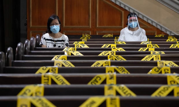 Women wearing protective masks kneel to pray in between social distancing markers placed on pews in St. Peter Parish, Metro Manila