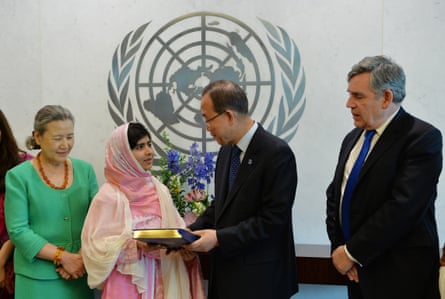 Malala Yousafzai dressed in a pink dress and head scarf at the UN headquarters in New York with Ban Ki-Moon presenting her with the charter, Gordon Brown on the far right and Ban’s wife Ban Soon-taek on the far left