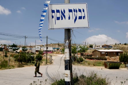 A soldier walks past a sign in Hebrew as white and blue flags fly overhead