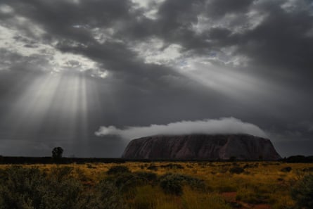 Sun rays shine through the clouds as the rain begins to retreat after morning rain over Uluru.