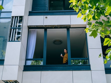 A woman drinking coffee in her apartment, photographed through broken window