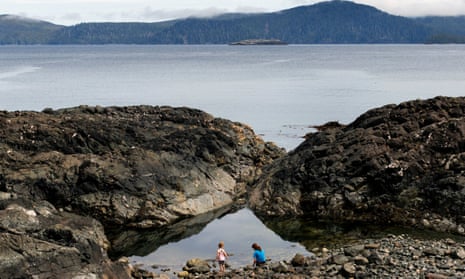 Two girls play on barnacle-covered rocks at SG̱ang Gwaay in British Columbia, Canada