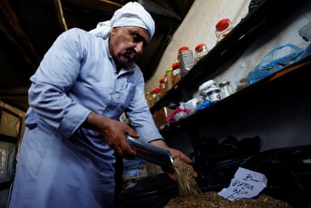 Muhanna shot from below scooping seeds next to shelf of bottles