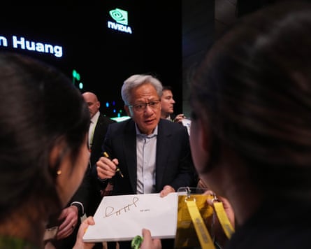 Jensen Huang holds a pen as a sheet of paper is held towards him.