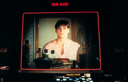 Closeup shot of a digital display for a live camera feed, showing Jim Carrey looking at himself in the mirror, with the illuminated text “ON AIR” above the display screen, and the text “TRUMAN HOUSE” below the screen