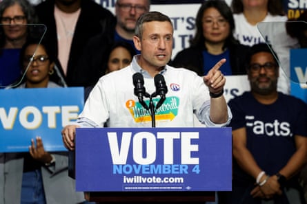 a man speaks into a microphone with a placard that reads ‘vote November 4’
