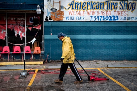 A man in a poncho drags a car jack as he walks in front of a storm-damaged tire shop.