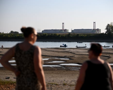 People standing in front of the power plant with dry river bed seen in front of them