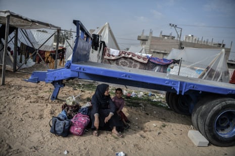 A Palestinian woman sits on a stone with a baby in a makeshift shelter in Rafah on 27 December.