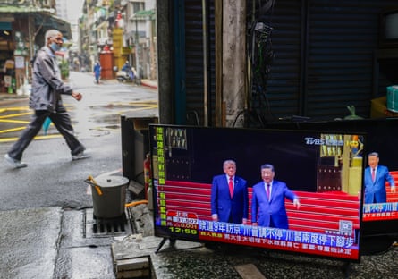 A pedestrian walks past a secondhand and TV repair store in Taipei, with TV screens broadcasting the Beijing meeting between Trump and Xi Jinping