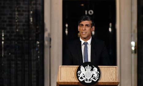Rishi Sunak pictured from the waist up, standing behind a lectern, with the No 10 front door visible in the background.