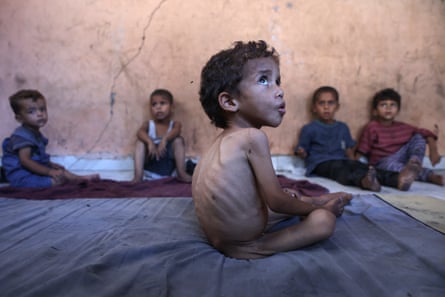 Starving little boy on a blanket with four other boys sitting with their backs to the wall