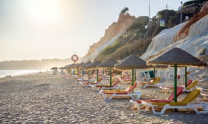 Chaises longues colorées sous des parasols en paille sur la plage de Falesia, Albufeira, Algarve, Portugal