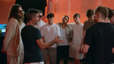 Simon Cowell talking to contestants who have arms around each other