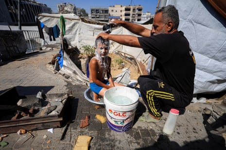 A Palestinian man, displaced by the Israeli offensive, bathes his son inside their shelter amid summer heat, in Gaza City.