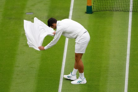 Novak Djokovic helps dry the court after a shower.