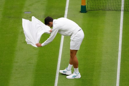Novak Djokovic membantu mengeringkan lapangan setelah diguyur hujan.