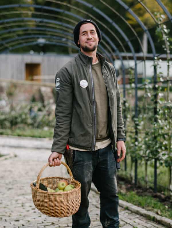 Un hombre lleva una canasta llena de manzanas y sonríe.