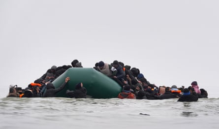 Dozens of people in shallow water trying to board an inflatable dinghy