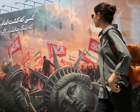 In Tehran, a woman walks past a mural depicting a toppled Statue of Liberty amid protest flags