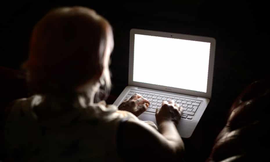 An anonymous woman sitting in the dark and using a laptop