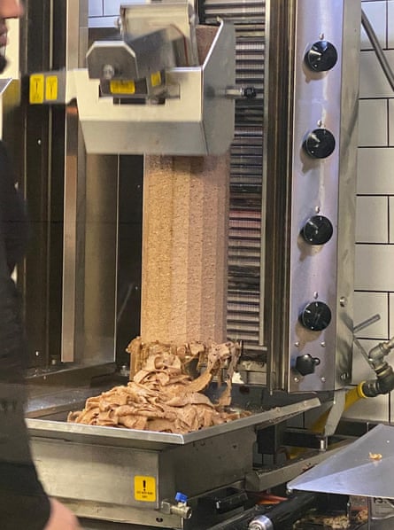 A machine shaves off slices of doner kebab meat, with strips of the meat piled up at the base