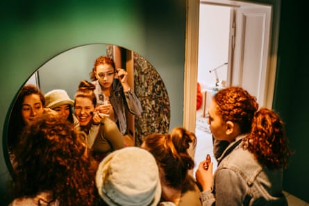 A group of young female friends applying makeup in front of a mirror