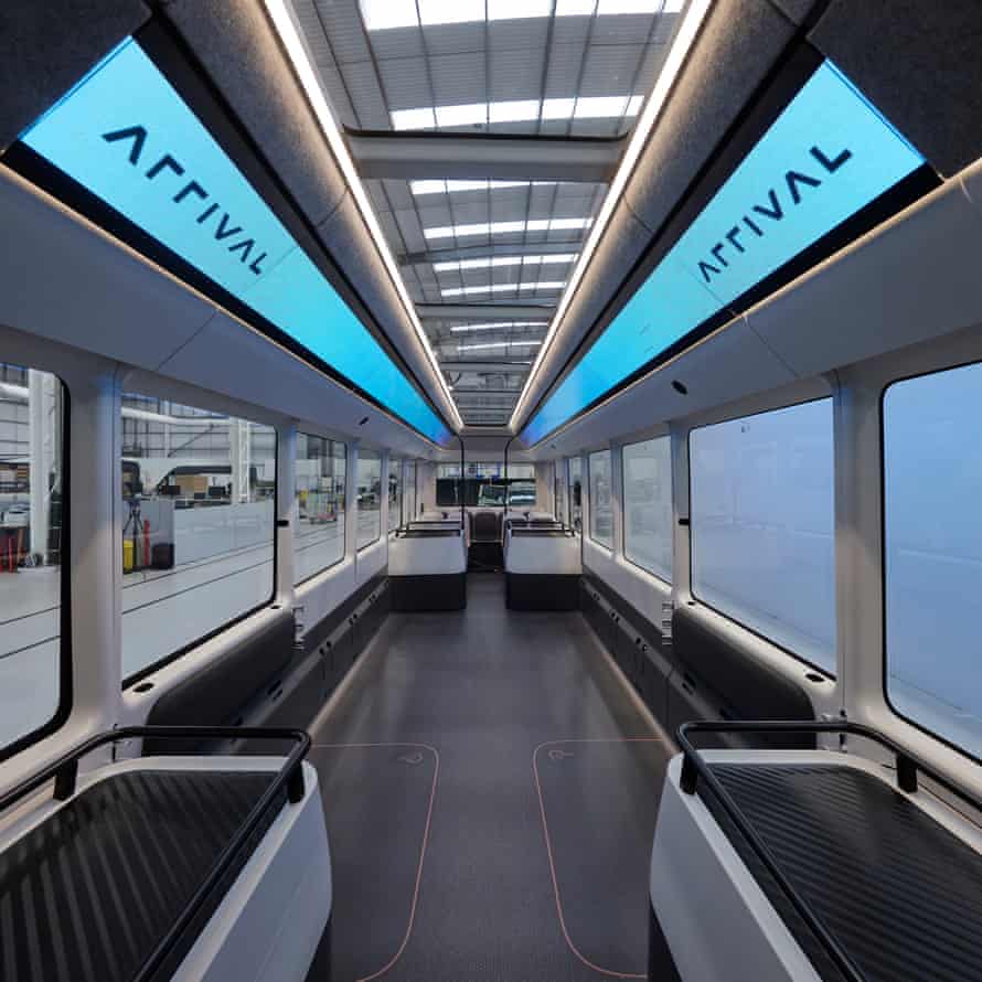 The futuristic, grey and white minimalist interior of the Arrival bus, with long roof mounted video screens and a lot of standing room