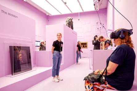 A woman sits wearing a VR headset in a pink-walled gallery; opposite her, behind glass, sits a self-portrait by Rembrandt