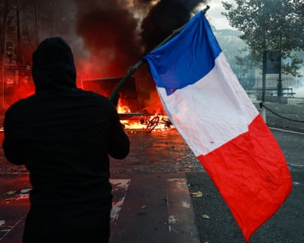 A protester holds a French flag before a burning barricade with thick black smoke