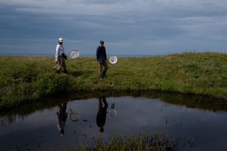 Two people with fishing nets on rods walk next to a body of water