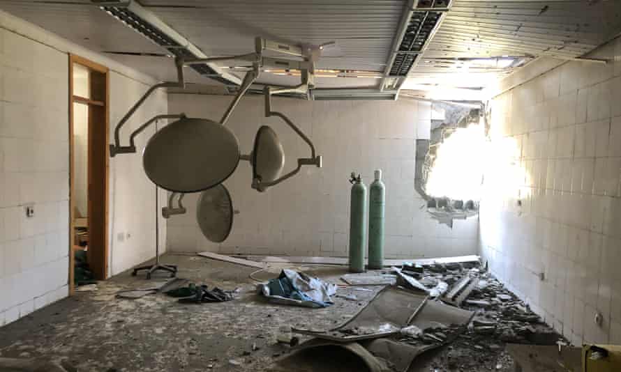 A wrecked operating room in a hospital with oxygen tanks and lights, and a large hole in the wall from shelling