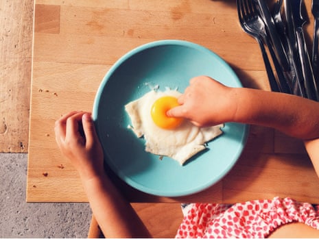 Girl's finger pressing into the yolk of a fried egg on a blue plate