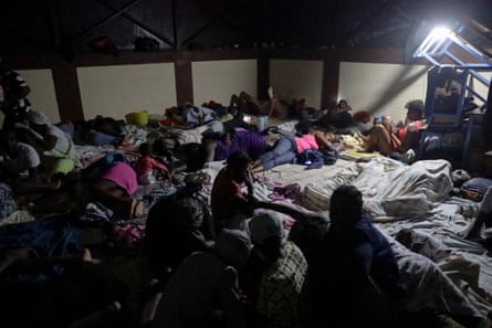 Lots of people sleeping on the floor of a classroom