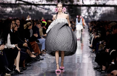 A model wearing a voluminous dress with what appears to be black lace overlaid on white, with white feather trim at the top