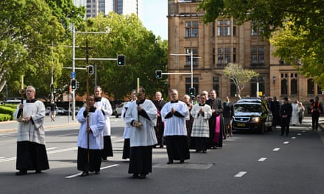 Procession on the street outside a cathedral showing priests walking in front of a hearse