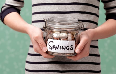 A person in a striped top holds a glass jar of coins labelled “Savings” with both hands