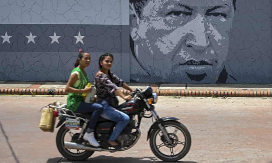 Two women ride past a mural with an image of late Venezuelan president Hugo Chavez in Sabaneta, Barinas State, Venezuela. 
