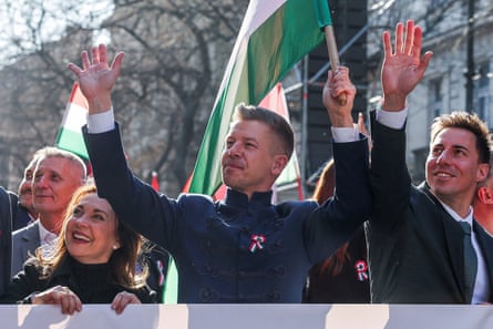 Péter Magyar smiles as he waves and holds up a Hungarian national flag next to others