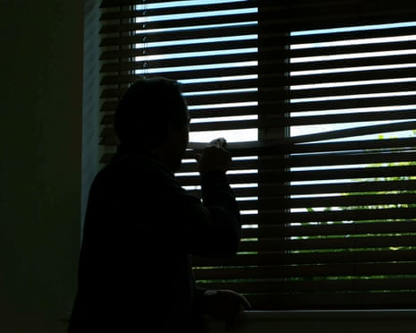An anonymous silhouetted figure looks out of a window with closed Venetian blinds